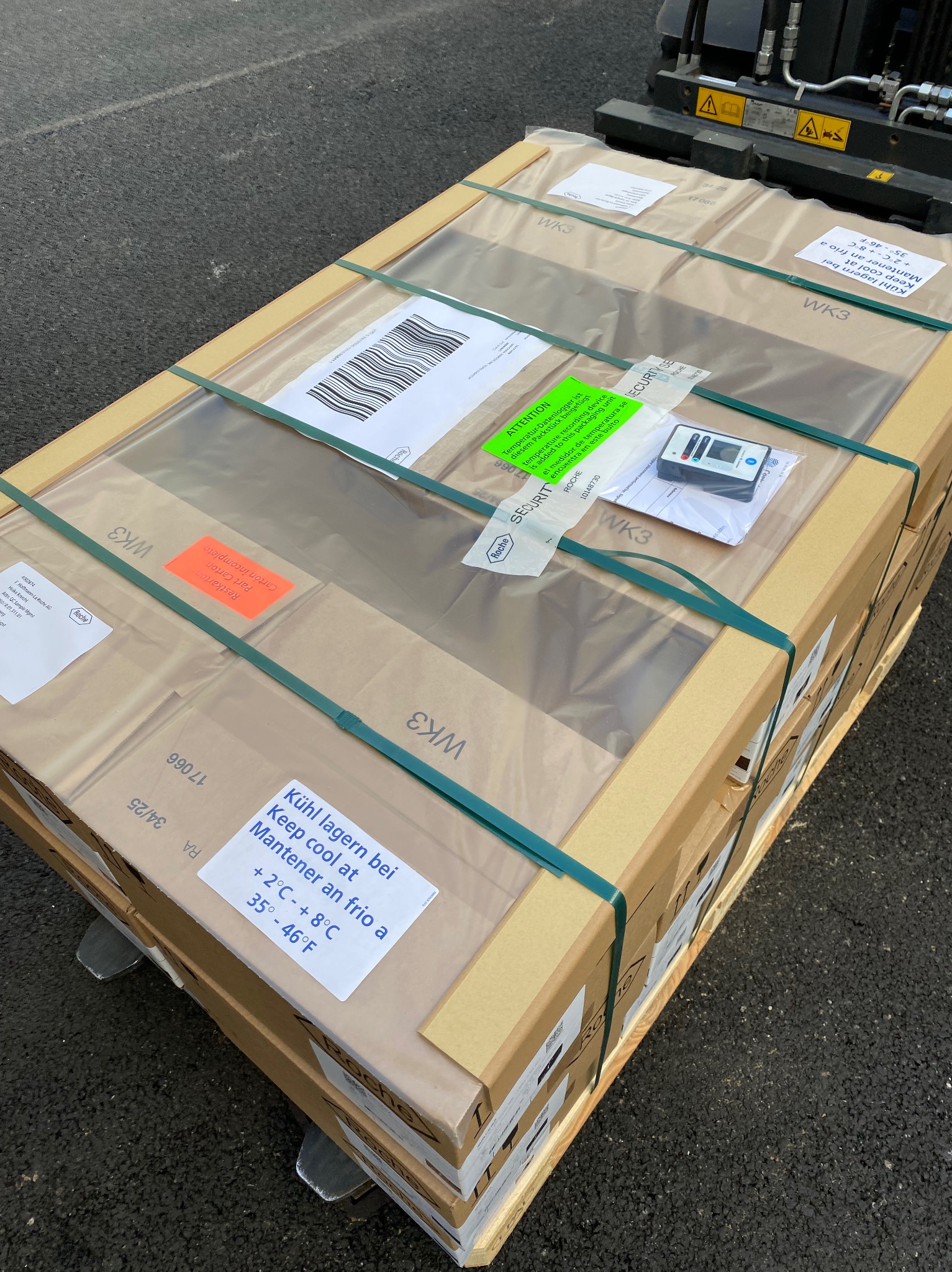 Paleta z kartonami WK3, zabezpieczona folią i taśmami, z etykietami informacyjnymi i urządzeniem do pomiaru temperatury, gotowa do transportu.