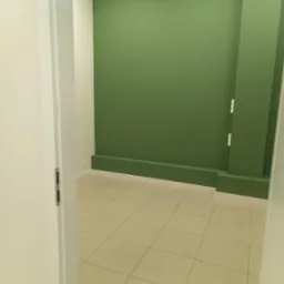 Pomalowane na zielono wnętrze z beżową podłogą z płytek, widoczne przez uchylone białe drzwi. Minimalistyczny design, świeżo po malowaniu.