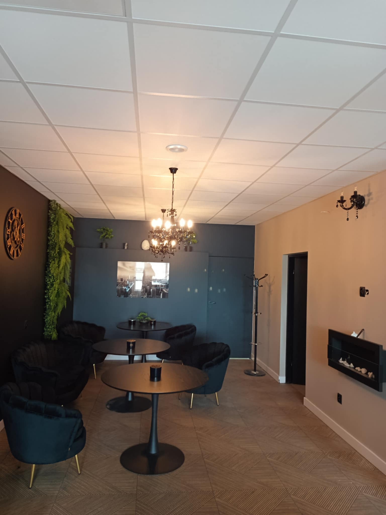 Eleganckie wnętrze kawiarni z czarnymi meblami, dekoracyjnym oświetleniem i roślinami. Parkiet ułożony we wzór jodełki. Ściany w odcieniach beżu i granatu.