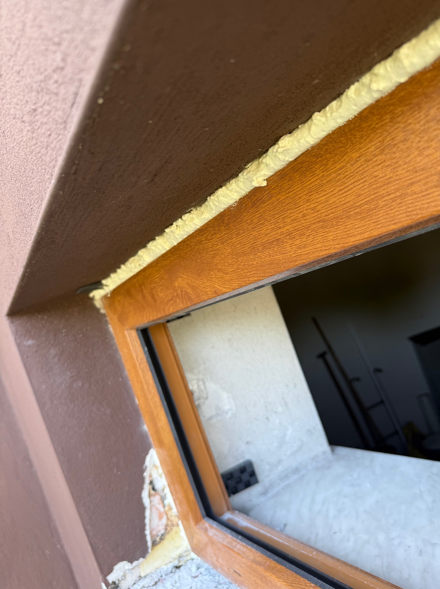 Montaż okna: brązowa rama z pianką montażową, widoczne uszkodzenia ściany. Ujęcie z bliska, podkreślające precyzję obróbki.