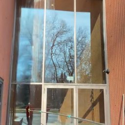 CzystoSPACE - Mycie wysokich okien budynku z użyciem lancy teleskopowej w Ząbkach. Widoczne odbicie drzew w szybach i drabina. Praca na wysokościach.