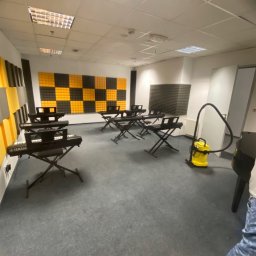 CzystoSPACE - Sala muzyczna z pianinami Yamaha i żółtym odkurzaczem. Akustyczne panele na ścianach. Szara wykładzina. Widok na salę podczas sprzątania.