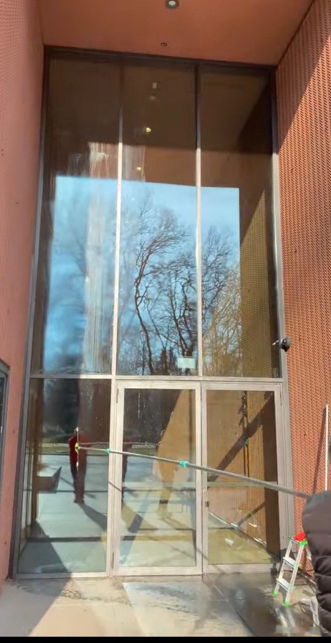 Mycie wysokich okien budynku z użyciem lancy teleskopowej w Ząbkach. Widoczne odbicie drzew w szybach i drabina. Praca na wysokościach.