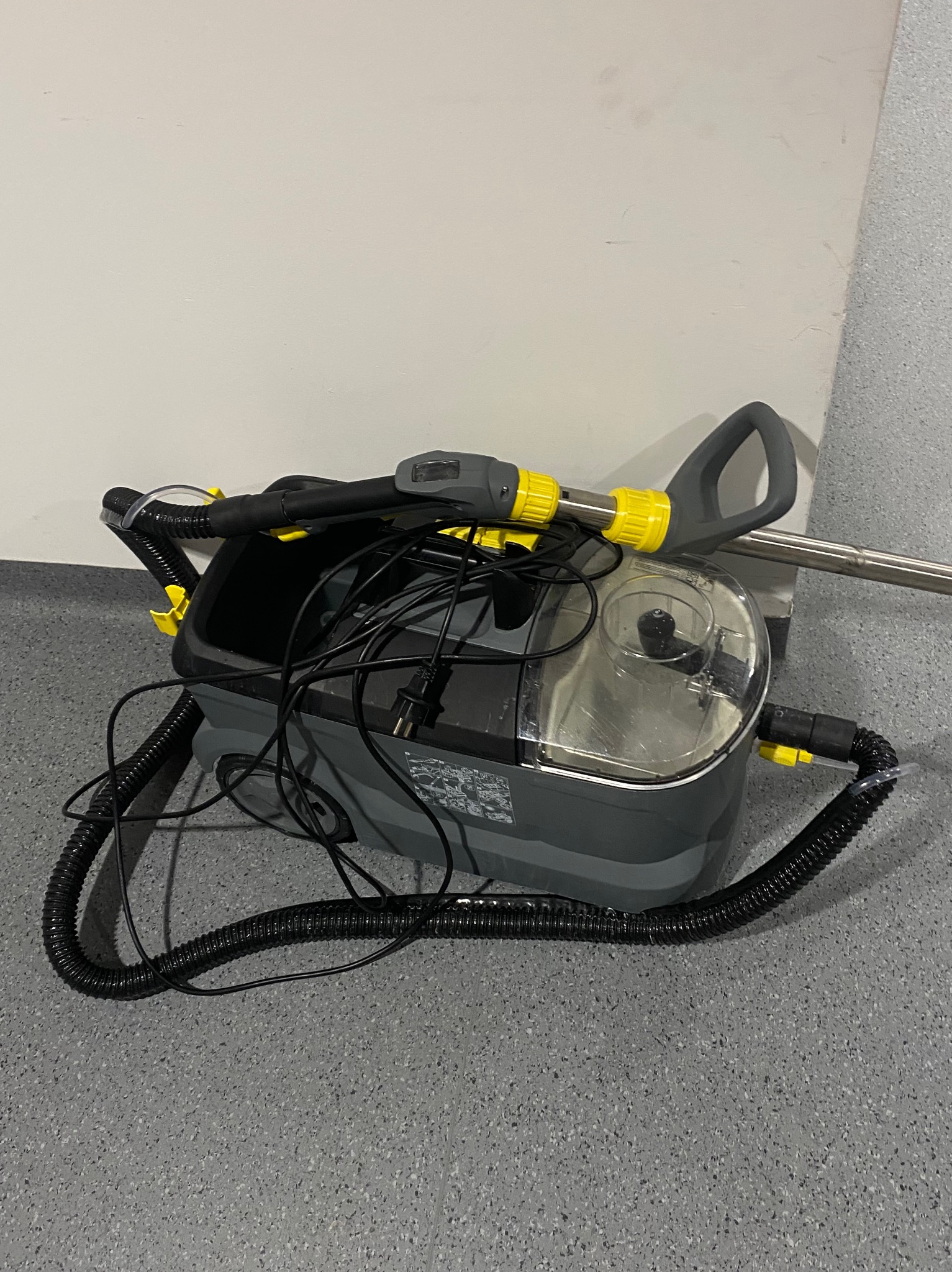 Profesjonalny odkurzacz piorący z żółtymi akcentami, gotowy do użycia na szarym tle. Widoczne przewody i elementy konstrukcyjne.