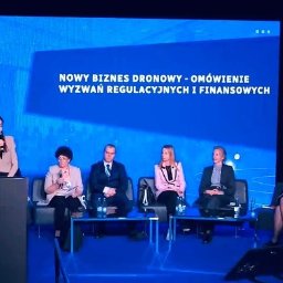 Marta Włodarczyk-Woźniczko Prawnik Przejęcia i finansowania spółek Corporate Governance Compliance Prawo bankowe - Konferencja o nowym biznesie dronowym: panel dyskusyjny z prelegentami na tle ekranu z tytułem. Kobieta przemawia zza mównicy, pozostali siedzą na krzesłach.