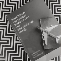 Marta Włodarczyk-Woźniczko Prawnik Przejęcia i finansowania spółek Corporate Governance Compliance Prawo bankowe - Książka 'Prawo lotnicze z perspektywy bezpieczeństwa' leży na wzorzystym tle, obok paszportu i modelu samolotu. Publikacja z zakresu prawa lotniczego.