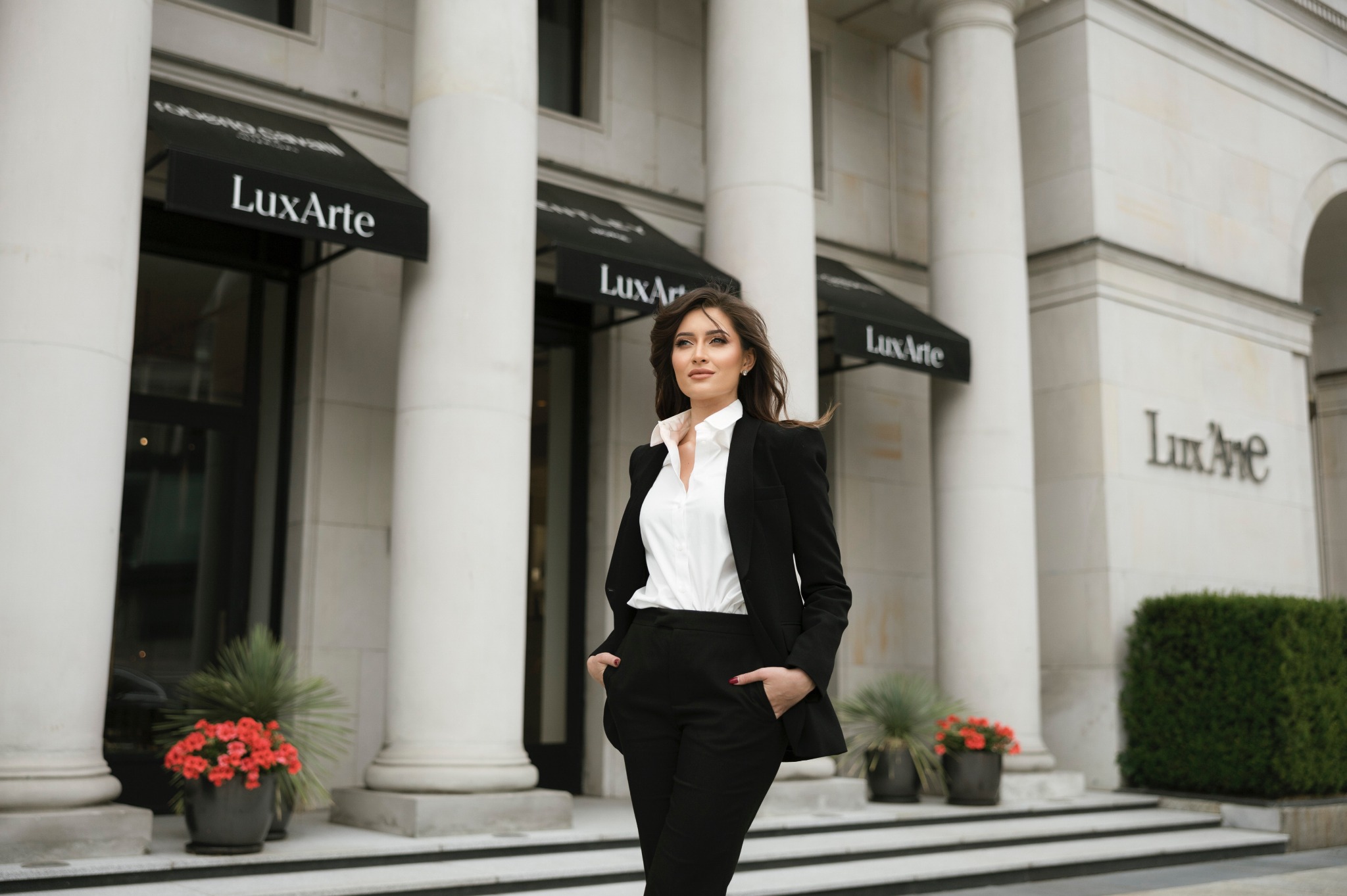 Profesjonalna prawniczka w czarnym garniturze, stojąca przed budynkiem z kolumnami i szyldem 'LuxArte', sugerująca elegancję i doświadczenie w obsłudze prawnej.