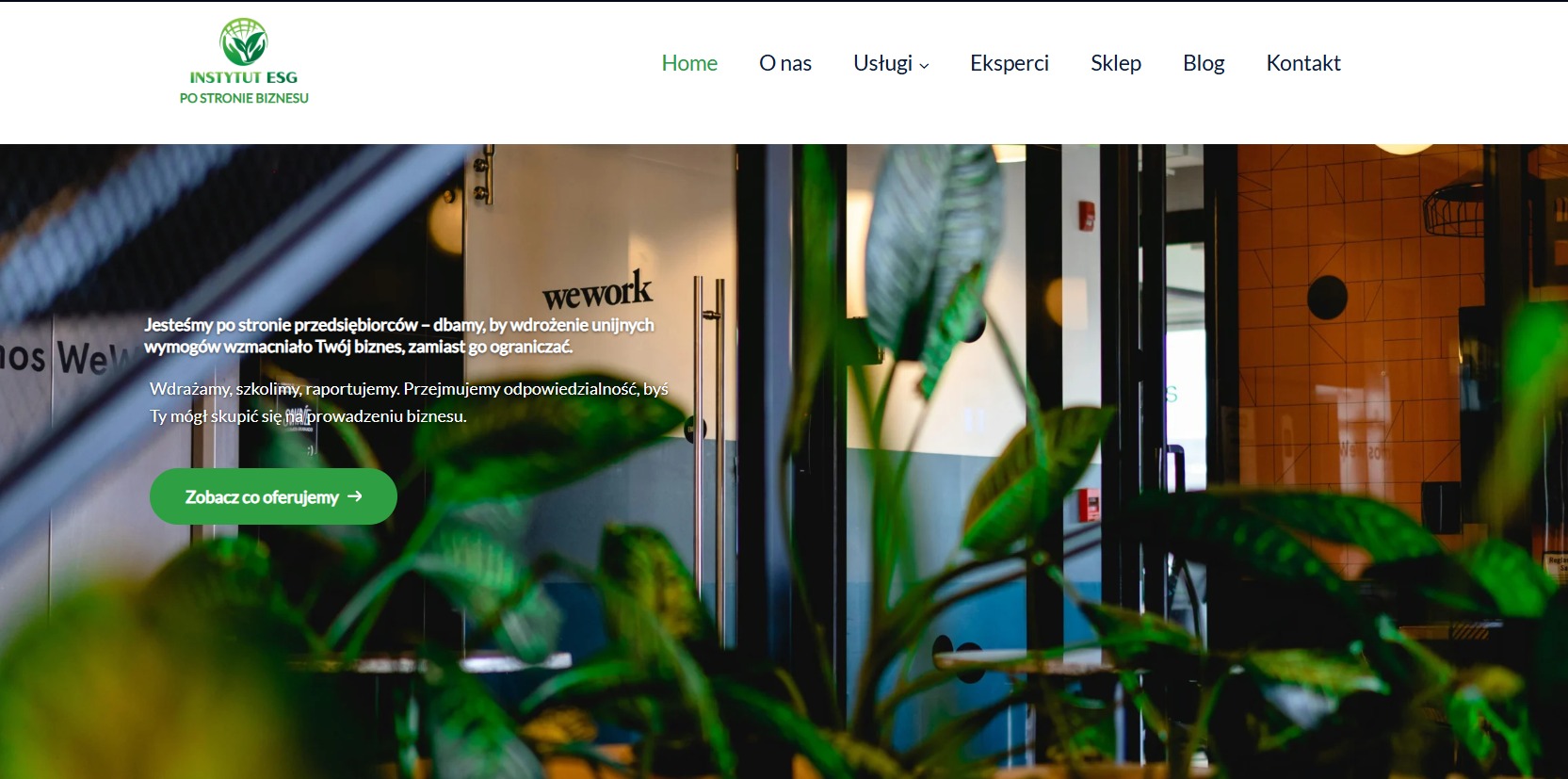 Strona internetowa Instytutu ESG z tekstem o wsparciu przedsiębiorców i wdrożeniu unijnych wymogów, widoczna przez rośliny doniczkowe w biurze WeWork.