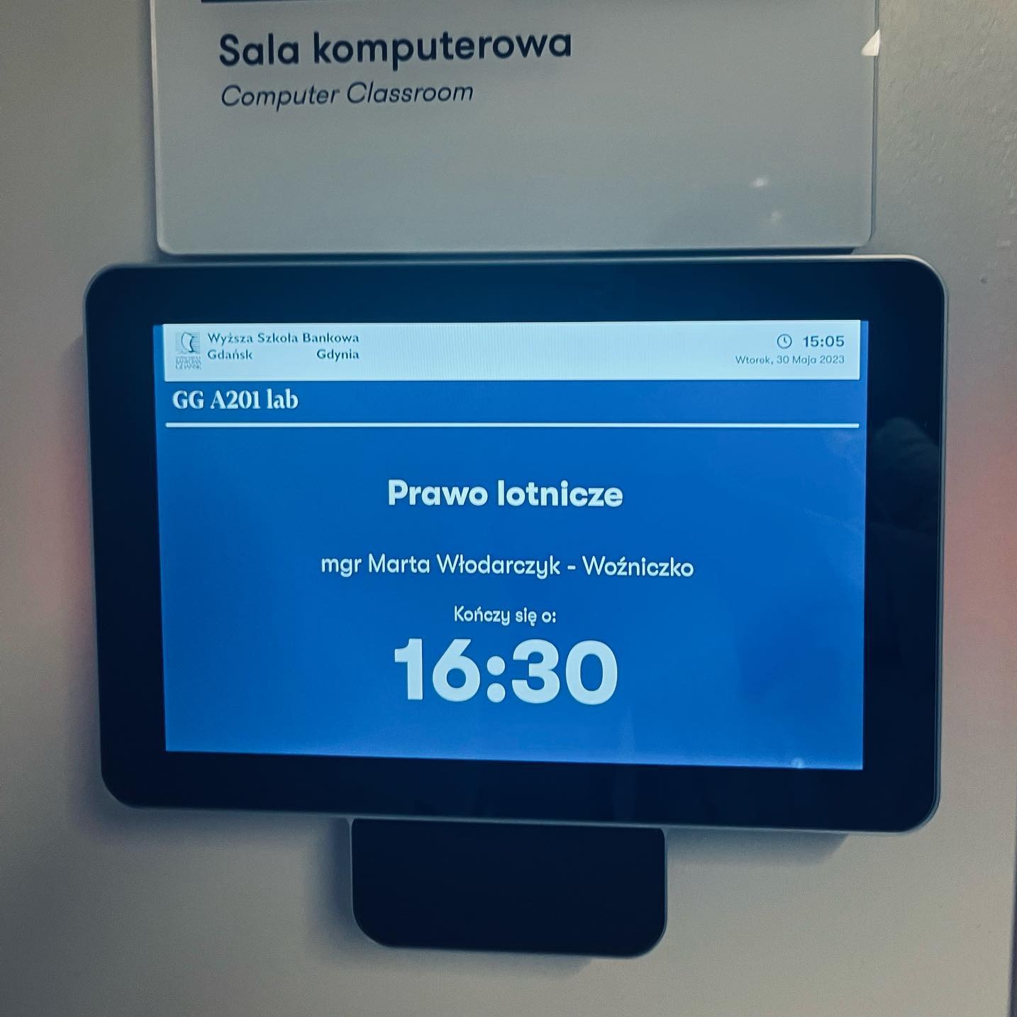 Ekran z informacją o wykładzie z prawa lotniczego w Gdańsku, prowadzonym przez mgr Martę Włodarczyk-Woźniczko, kończącym się o 16:30, w sali komputerowej.