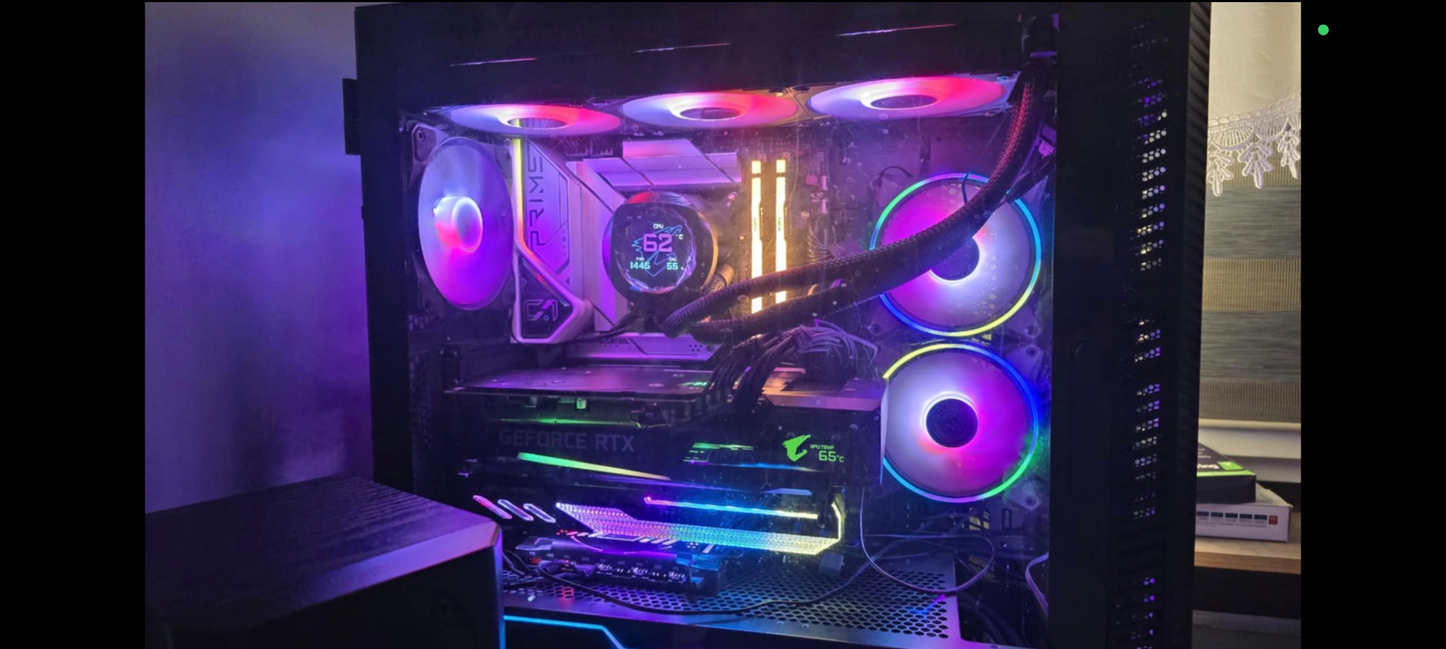 Komputer stacjonarny z podświetleniem RGB, widoczna karta graficzna GeForce RTX i chłodzenie wodne z wyświetlaczem temperatury CPU. Obudowa typu tower, wentylatory z kolorowym podświetleniem.