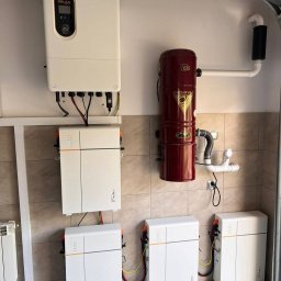 IQDOM24 Sp. z o.o. - Instalacja magazynów energii Triple Power z inwerterem Solax w garażu, widoczne okablowanie i elementy montażowe. Ujęcie z dołu, podkreślające profesjonalny montaż.