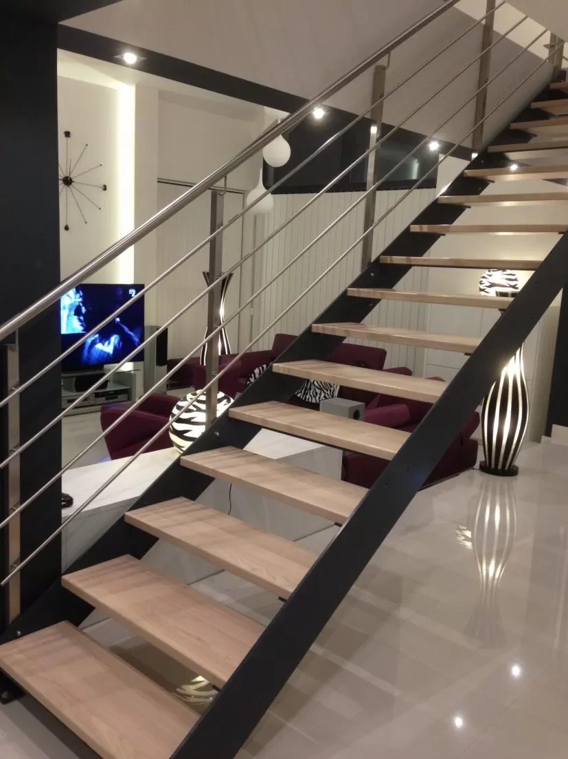 Nowoczesne schody z drewnianymi stopniami i metalową konstrukcją, widoczne z dołu, z salonem w tle. Minimalistyczny design, jasne oświetlenie.