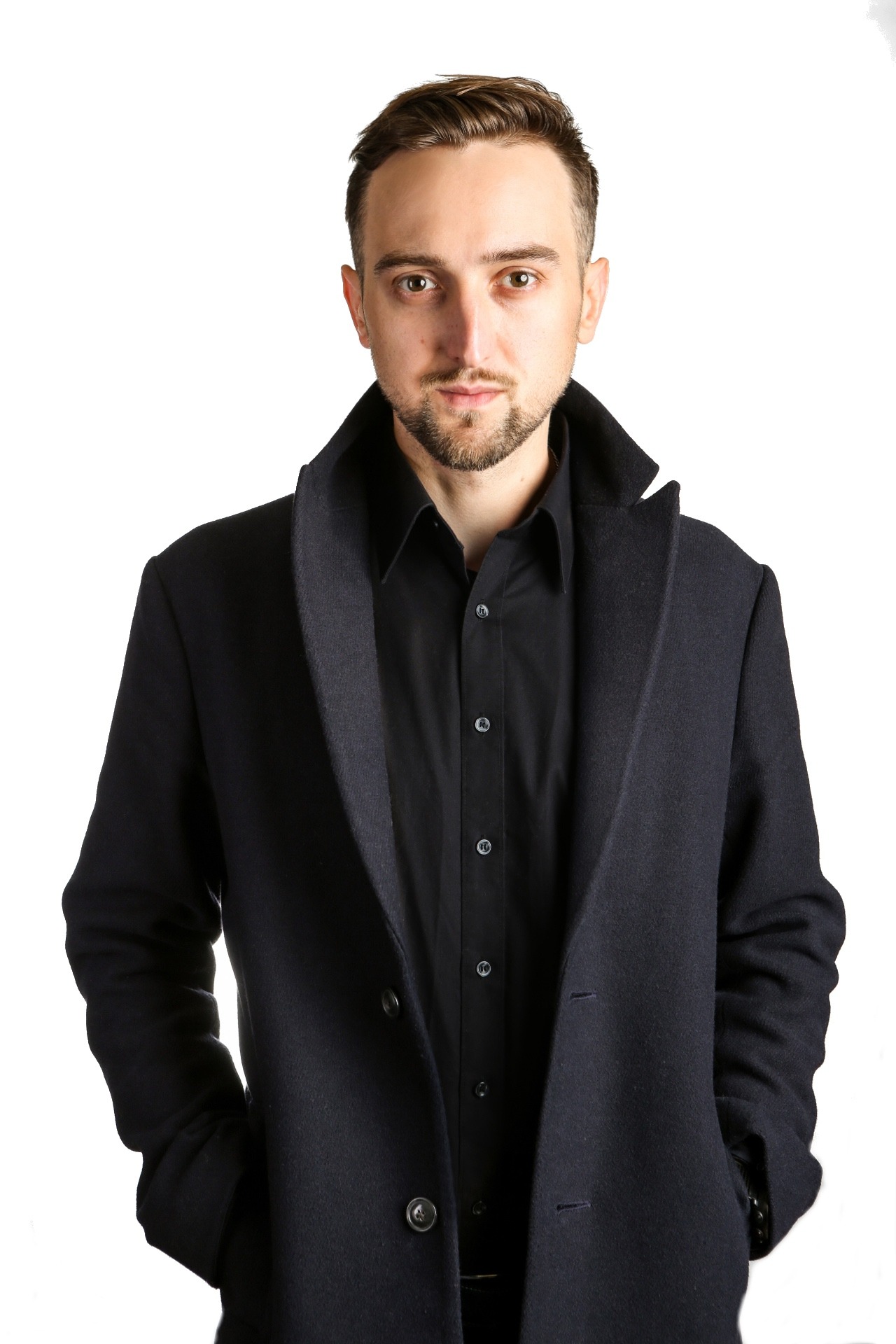Portret mężczyzny w czarnej koszuli i płaszczu na białym tle. Uśmiech, broda, brązowe oczy. Profesjonalny wizerunek lektora języka angielskiego.