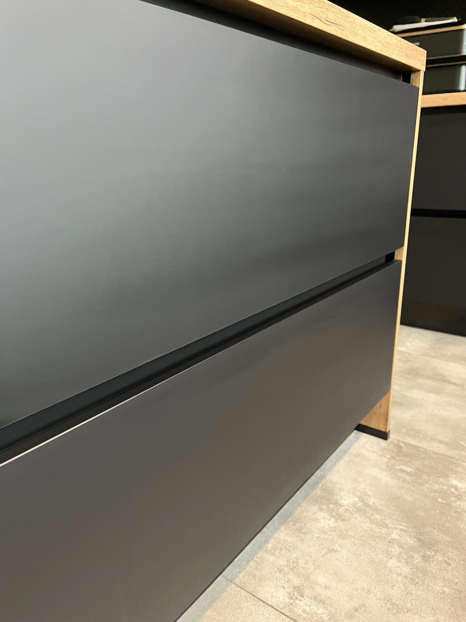 Nowoczesna szafka z szufladami w odcieniach szarości i drewna, widoczna z bliska pod kątem, ukazująca minimalistyczny design i gładkie powierzchnie.