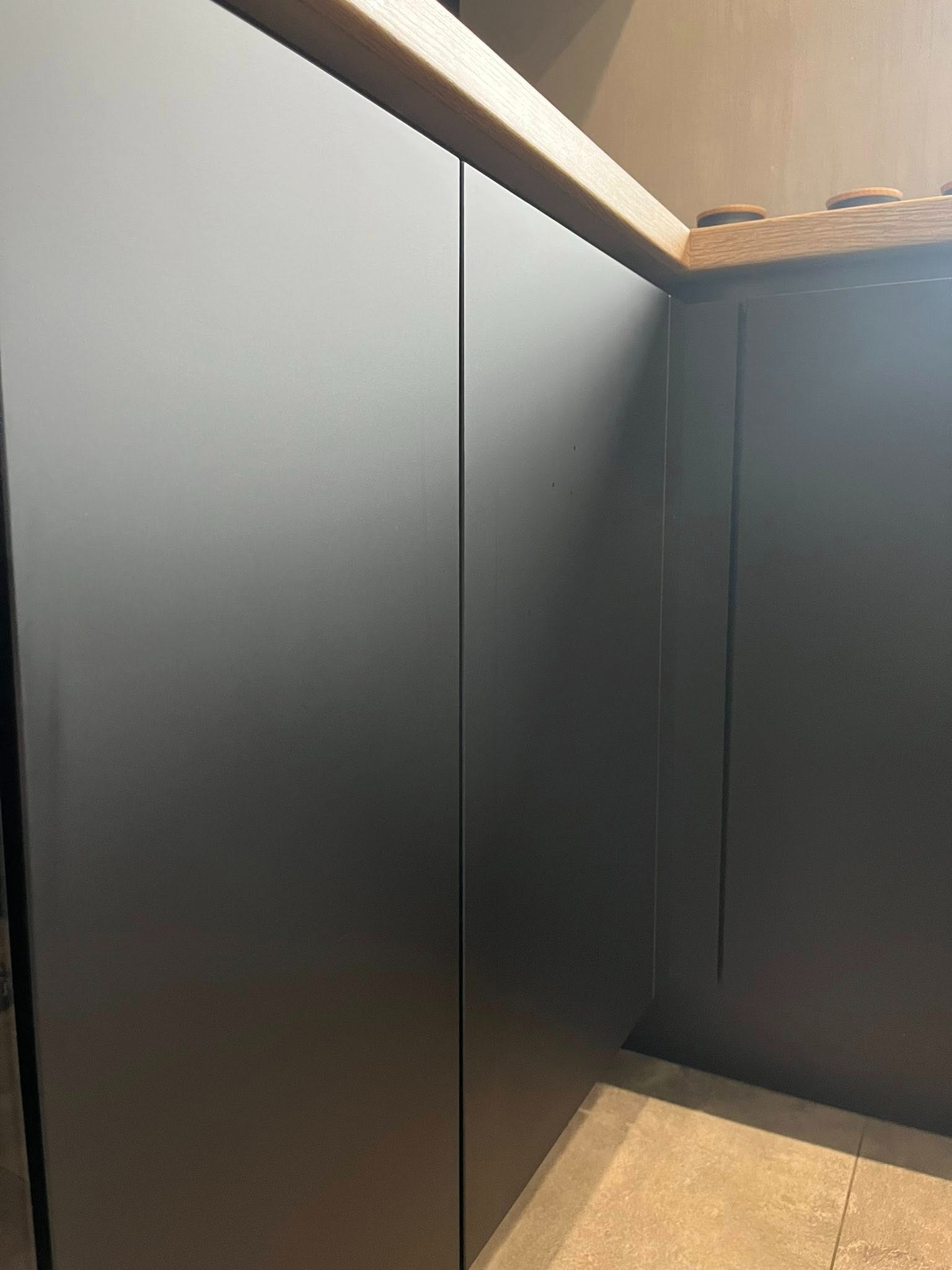 Szare, matowe fronty szafek kuchennych z drewnianym blatem, widoczne z bliskiej perspektywy, ukazujące detale wykończenia i minimalistyczny design.