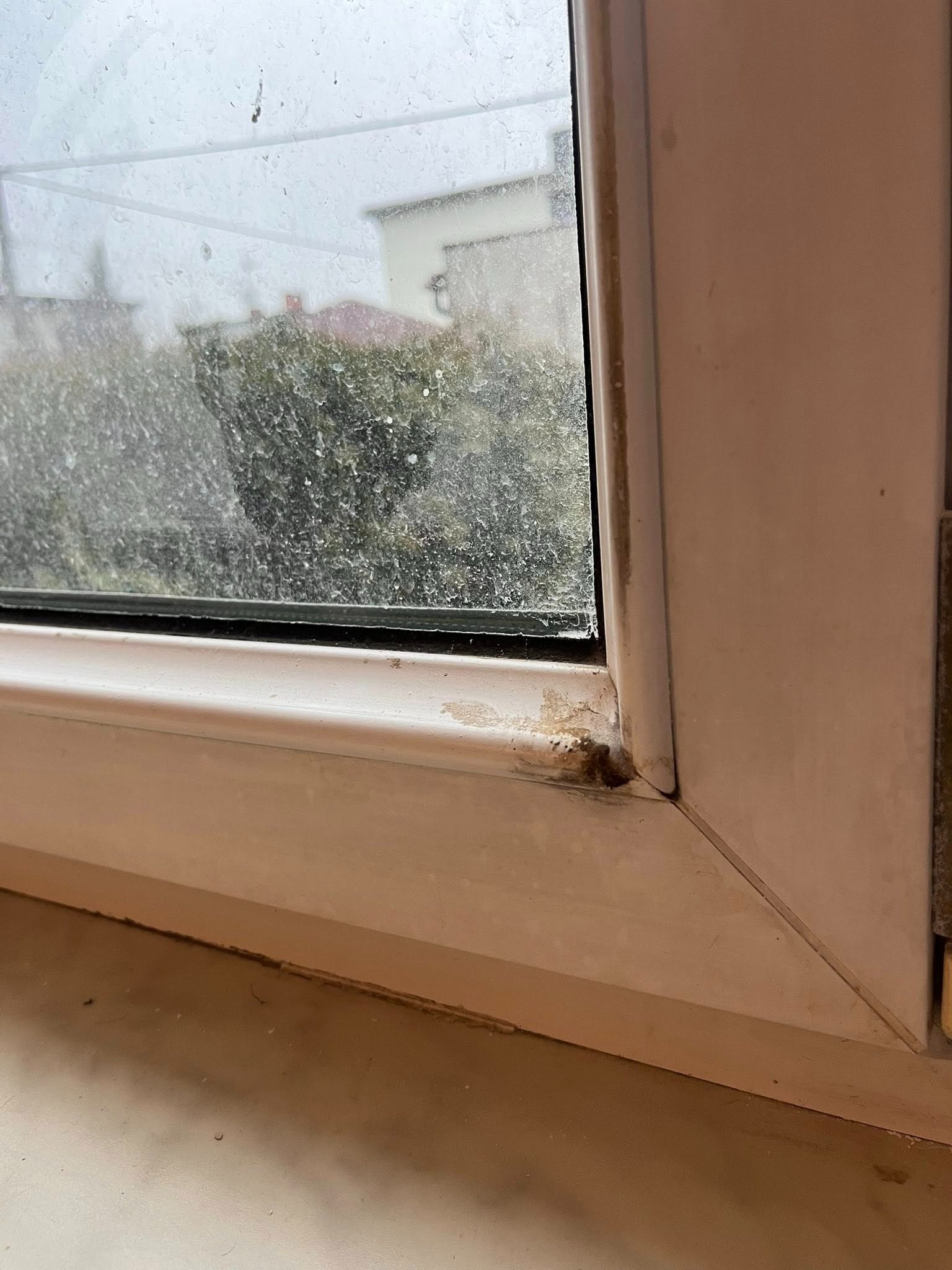 Brudne okno PCV z widocznymi plamami i zabrudzeniami na szybie oraz ramie, wymagające czyszczenia. Widok z bliska na narożnik okna.