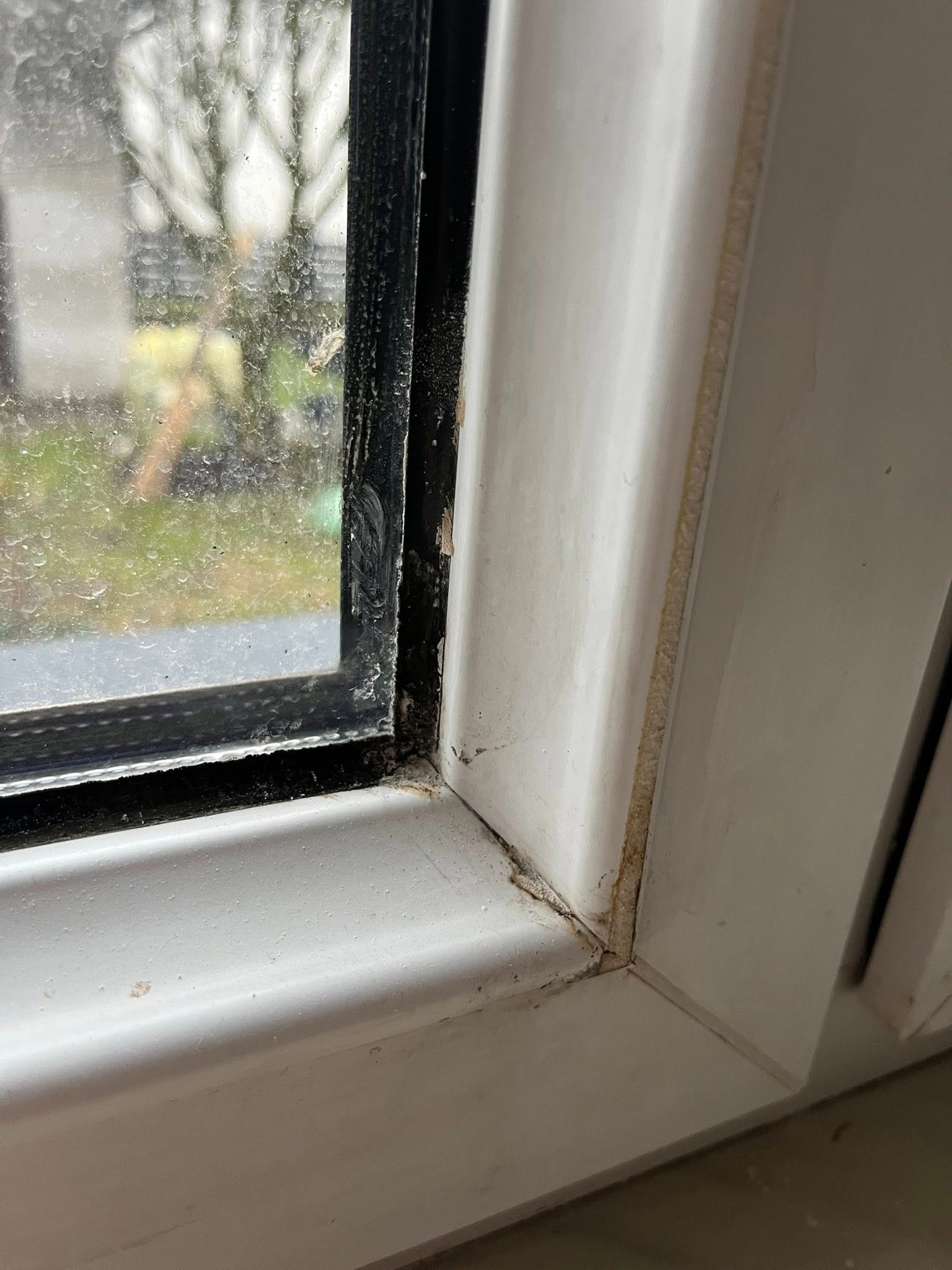 Brudne okno PCV z widocznymi zabrudzeniami na szybie i ramie, ukazane w zbliżeniu. Widoczne ślady kurzu i wilgoci w narożnikach ramy okiennej.