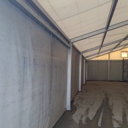 SkyDan - Wnętrze hali z metalową konstrukcją i płóciennymi ścianami. Świeżo wylana, mokra posadzka. Widok w głąb hali, oświetlenie naturalne i sztuczne.