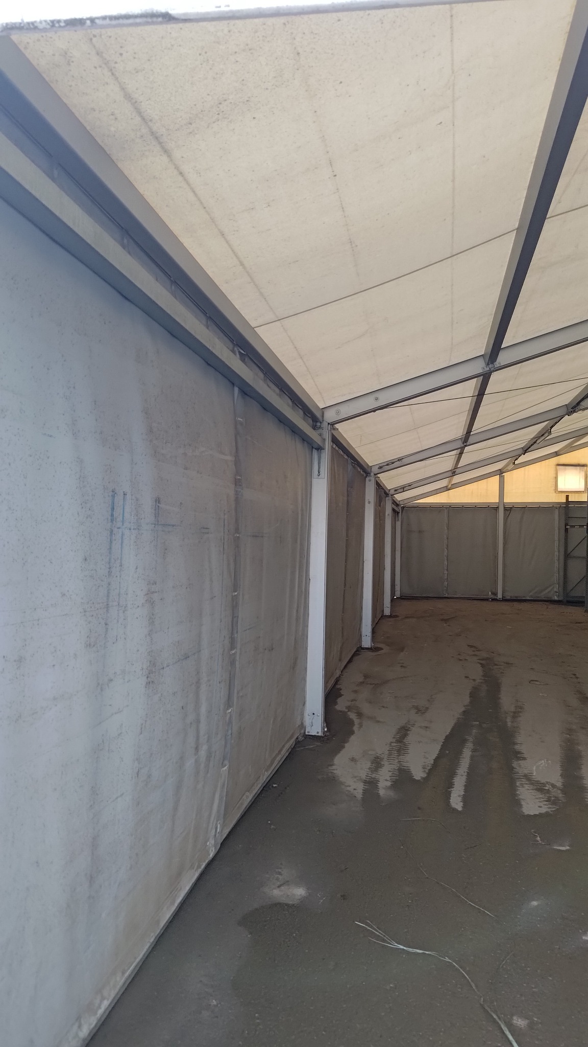 Wnętrze hali z metalową konstrukcją i płóciennymi ścianami. Świeżo wylana, mokra posadzka. Widok w głąb hali, oświetlenie naturalne i sztuczne.