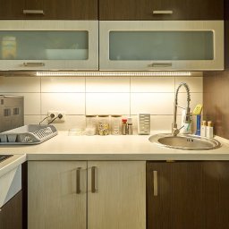 Mateusz Bojdoł - Jasna kuchnia z drewnianymi szafkami, oświetleniem LED pod szafkami i srebrnym zlewem. Na blacie widoczne akcesoria kuchenne i ekspres do kawy.