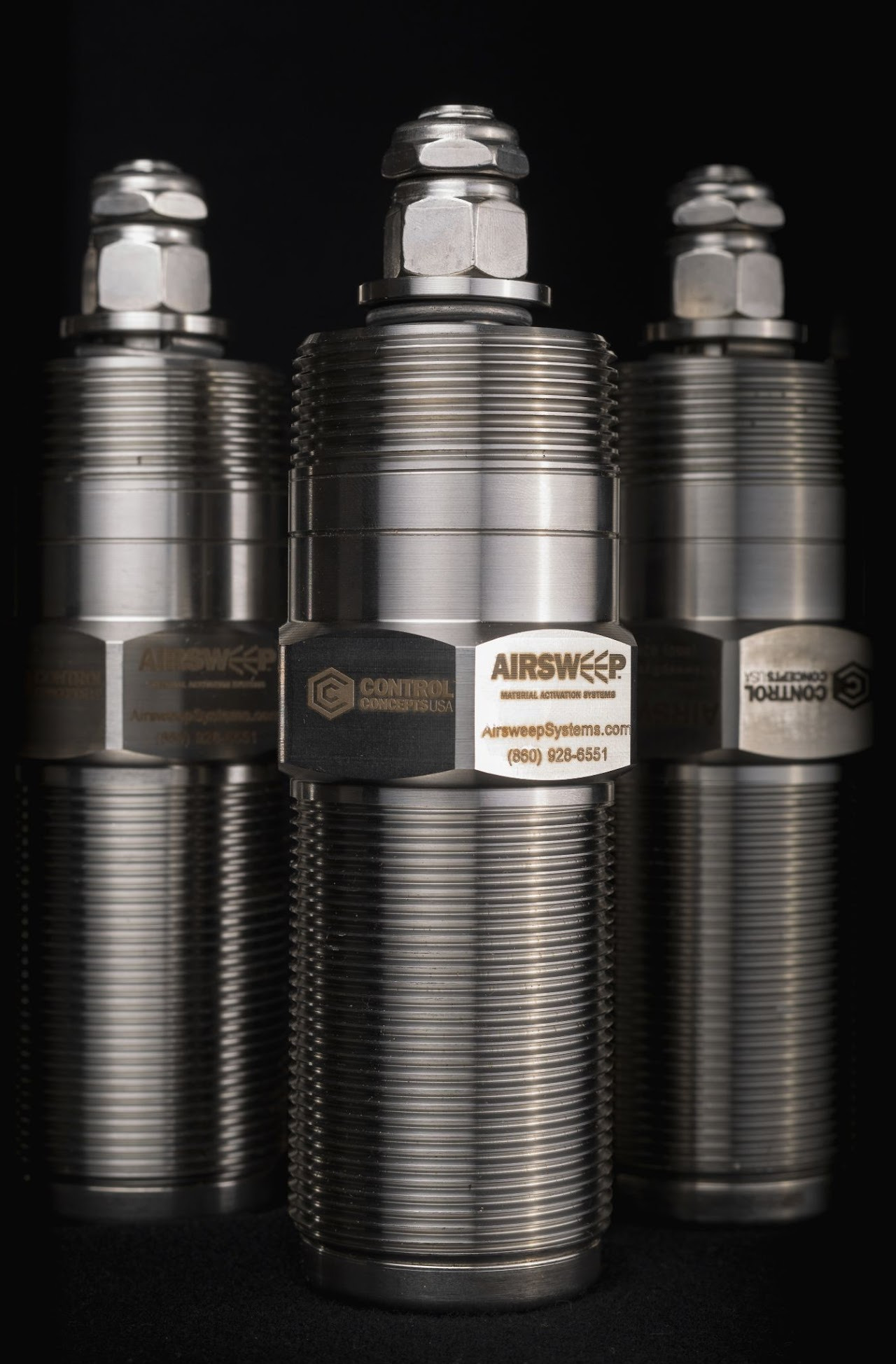 Trzy metalowe cylindryczne urządzenia Airsweep z logo i danymi kontaktowymi na czarnym tle, oświetlone studyjnie, prezentujące detale gwintowania i wykończenia.