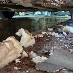 Car Body Design Krzysztof Krzywicki - Uszkodzone podwozie samochodu na podnośniku w warsztacie, widoczne fragmenty skorodowanej blachy i pianki montażowej. Niefachowa naprawa antykorozyjna.