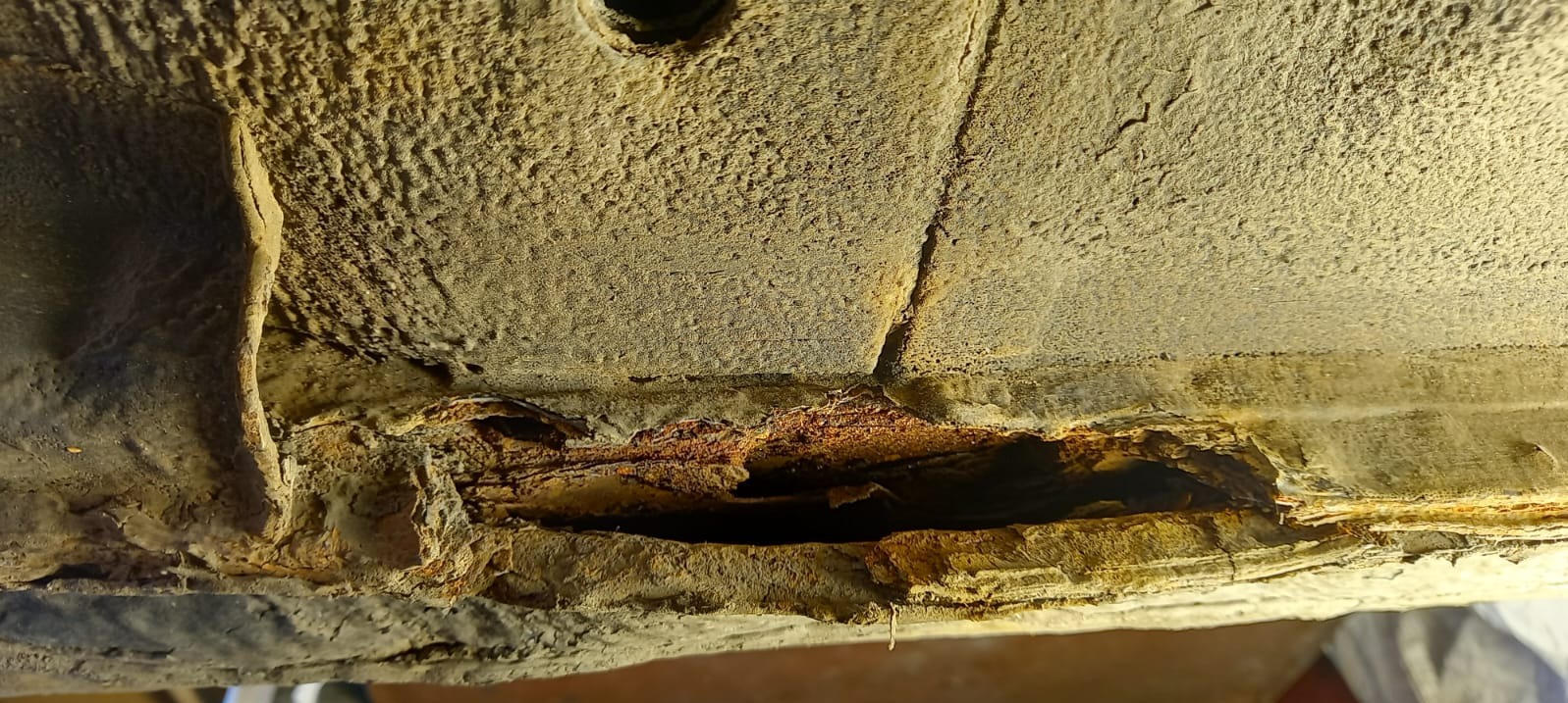 Korozja podwozia samochodu z widocznymi ubytkami i rdzawym nalotem. Szczegółowe ujęcie uszkodzeń, podkreślające stopień zaawansowania korozji.