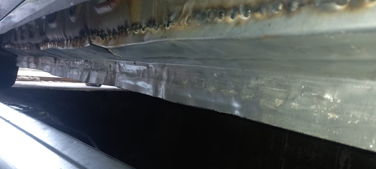 Detal podwozia samochodu po spawaniu, widoczne ślady spawów i napraw blacharskich. Metaliczna powierzchnia z widocznymi nierównościami i śladami obróbki.