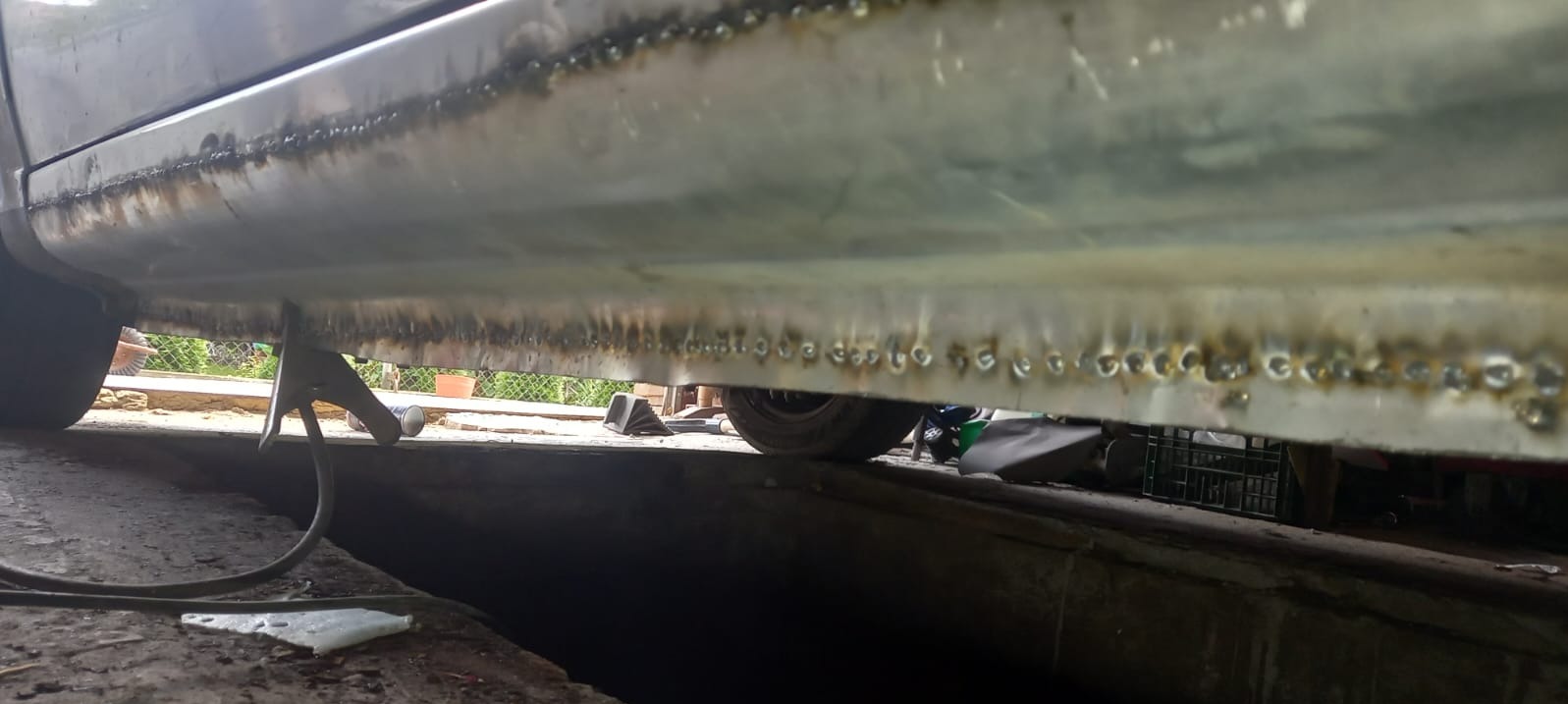 Detal progu samochodu po spawaniu, widoczne punkty spawów. Auto podparte na podnośniku, w tle opona i elementy warsztatu.