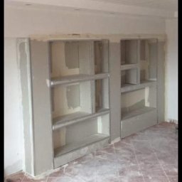 Home & Trade Tomasz Gliński - Dwa wnękowe regały z płyt karton-gips na ścianie, w trakcie szpachlowania i wygładzania, widoczne płytki na podłodze, sufit podwieszany.