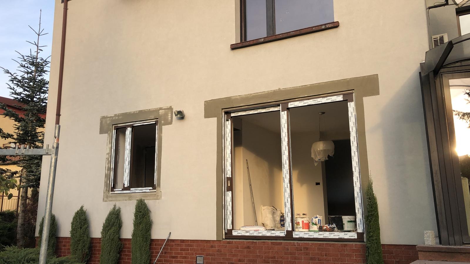 Dom jednorodzinny z oknami po montażu, z widocznymi śladami prac murarskich wokół ram okiennych. Na pierwszym planie widoczne materiały budowlane.