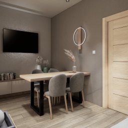 IDK interiors - Nowoczesna jadalnia z drewnianym stołem i szarymi krzesłami. Na ścianie telewizor i okrągła lampa. Minimalistyczny design, ciepłe oświetlenie, parkiet na podłodze.