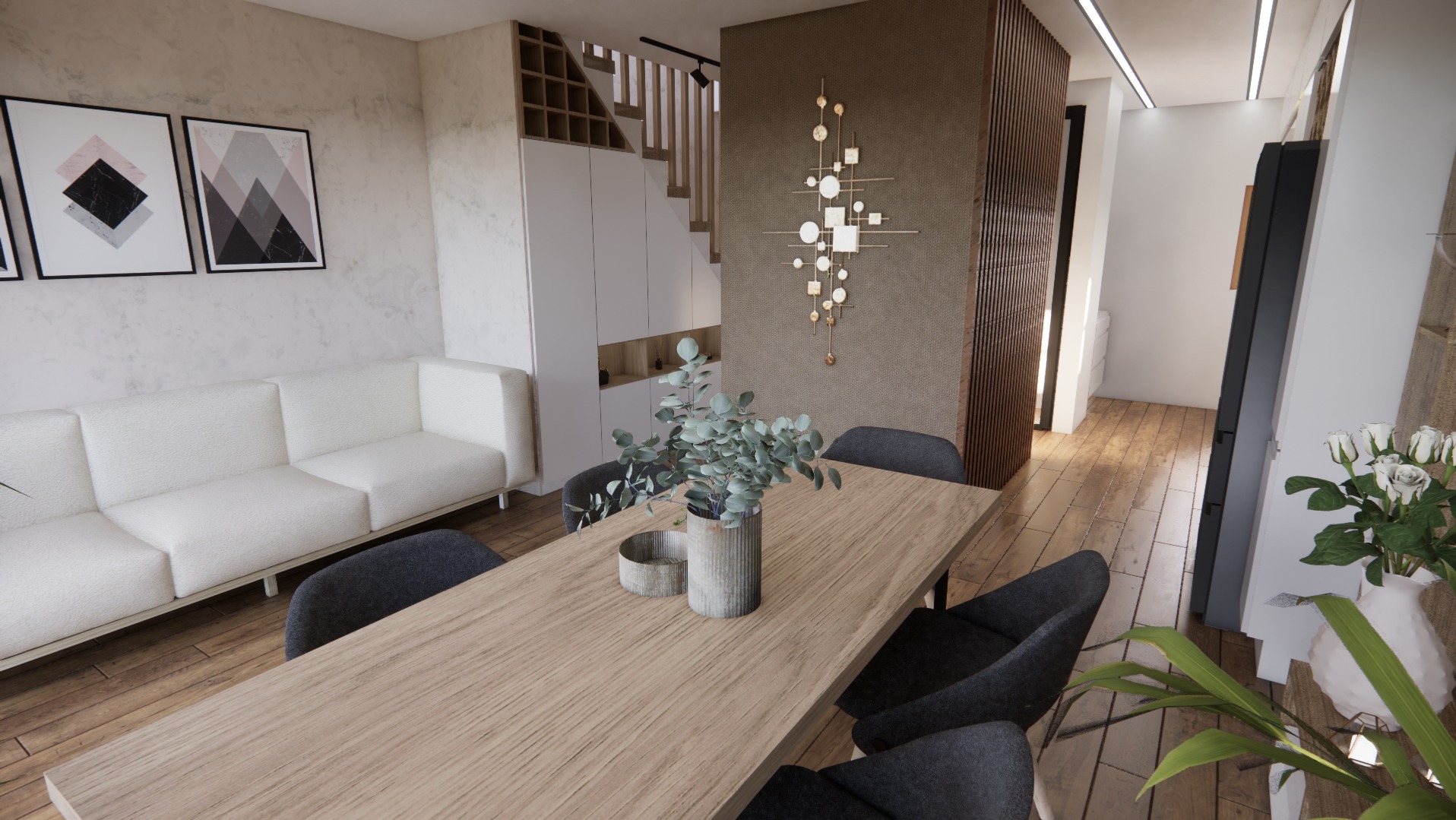 Jasne wnętrze z drewnianym stołem, szarą tapicerką krzeseł i białym narożnikiem. Na ścianie abstrakcyjna dekoracja. Widoczne schody i rośliny doniczkowe.