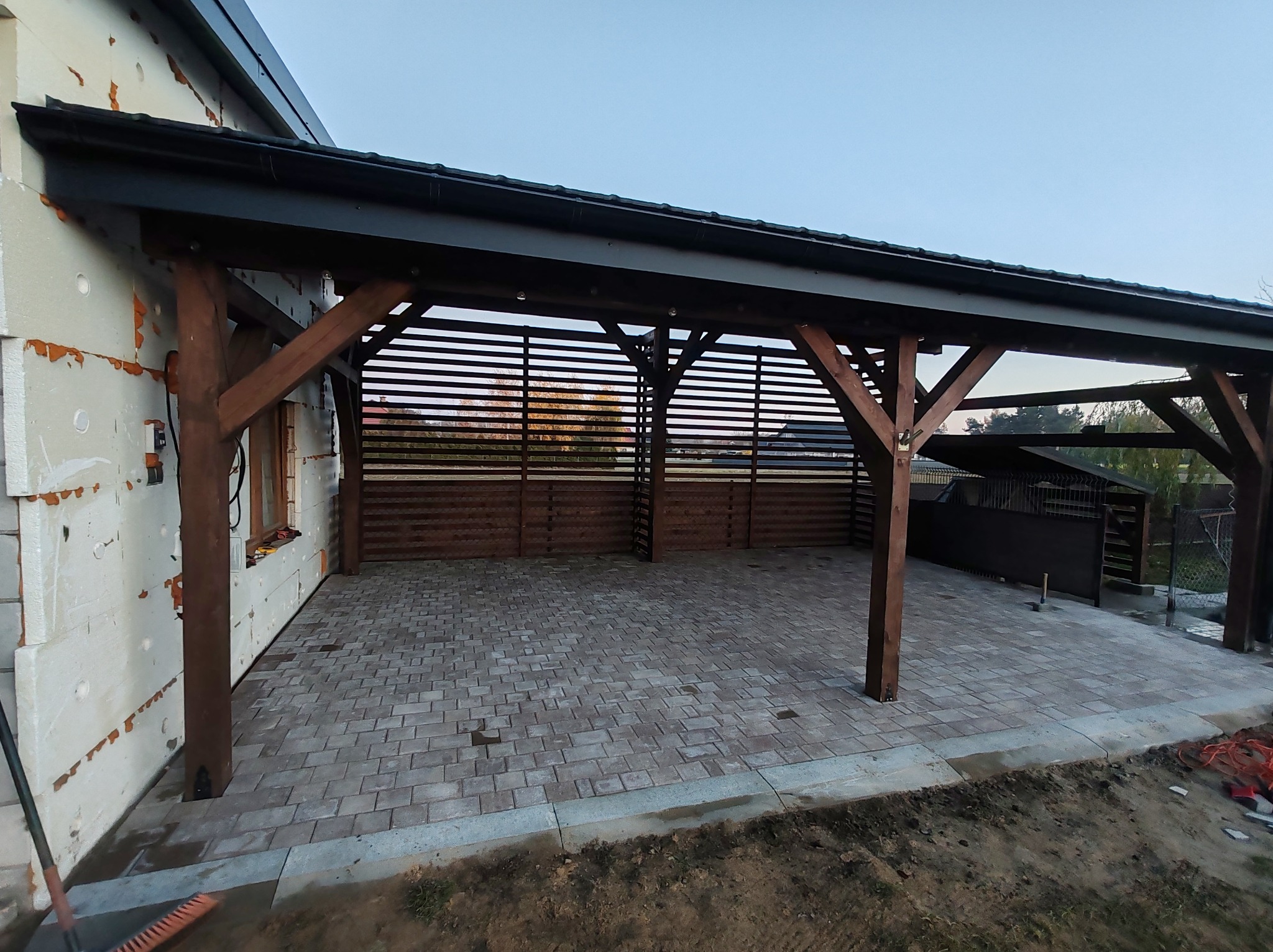 Zadaszenie tarasu z drewnianą konstrukcją i kostką brukową w odcieniach szarości. Widoczne detale wykończenia i elementy konstrukcyjne.