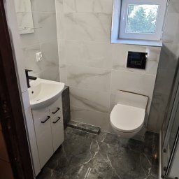 Rafał Muller LOGOS - Wykończona łazienka z umywalką na szafce, toaletą typu Geberit i kabiną prysznicową. Marmurowe płytki na ścianach i podłodze. Nowoczesny design.