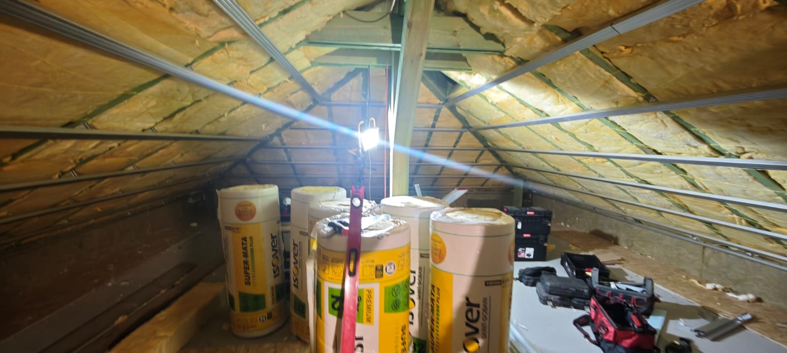 Ocieplenie poddasza wełną mineralną Isover Super-Mata, widoczne profile metalowe i narzędzia. Prace wykończeniowe na poddaszu, izolacja termiczna dachu.