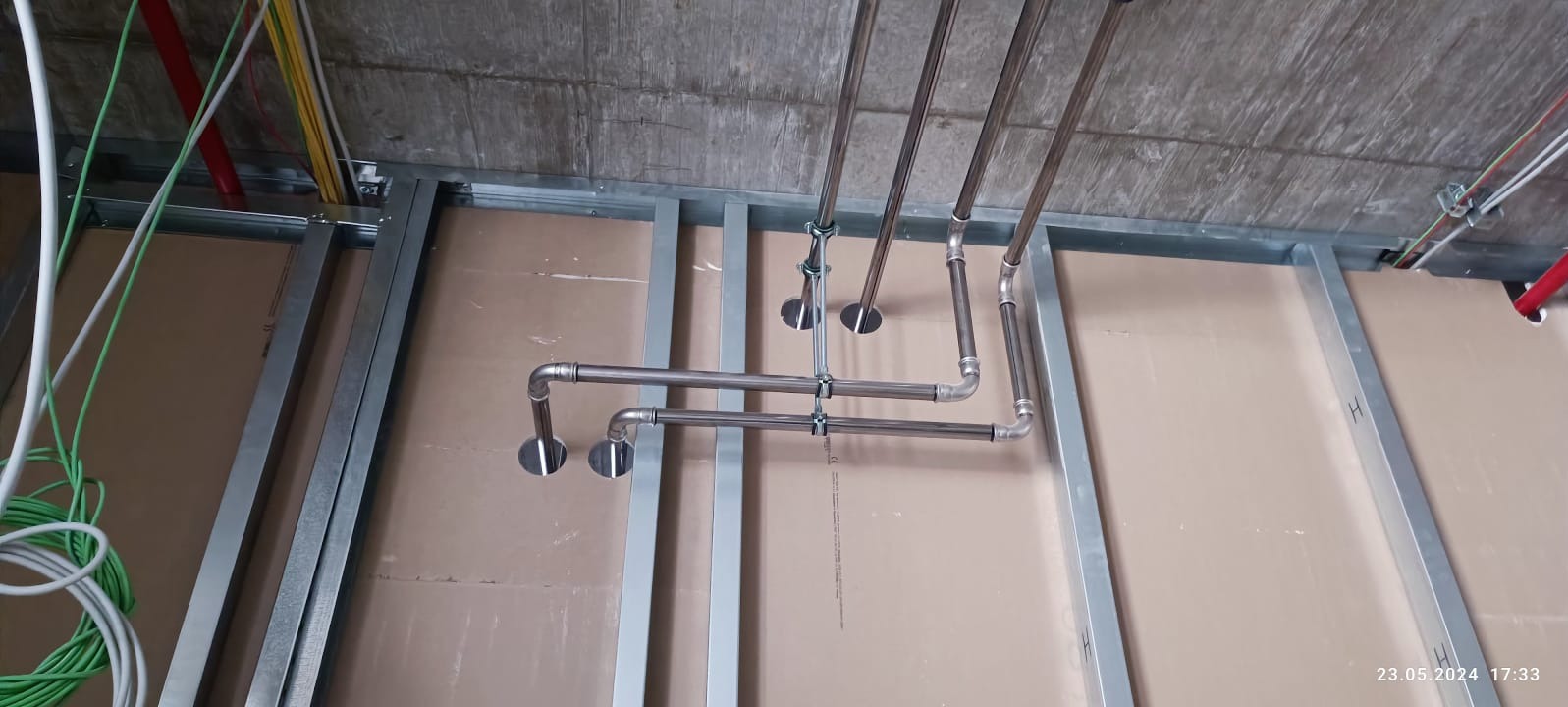 Metalowa konstrukcja sufitu podwieszanego z instalacją rur, widoczne przewody elektryczne i płyty kartonowo-gipsowe. Ujęcie z dołu, surowy stan wykończenia.