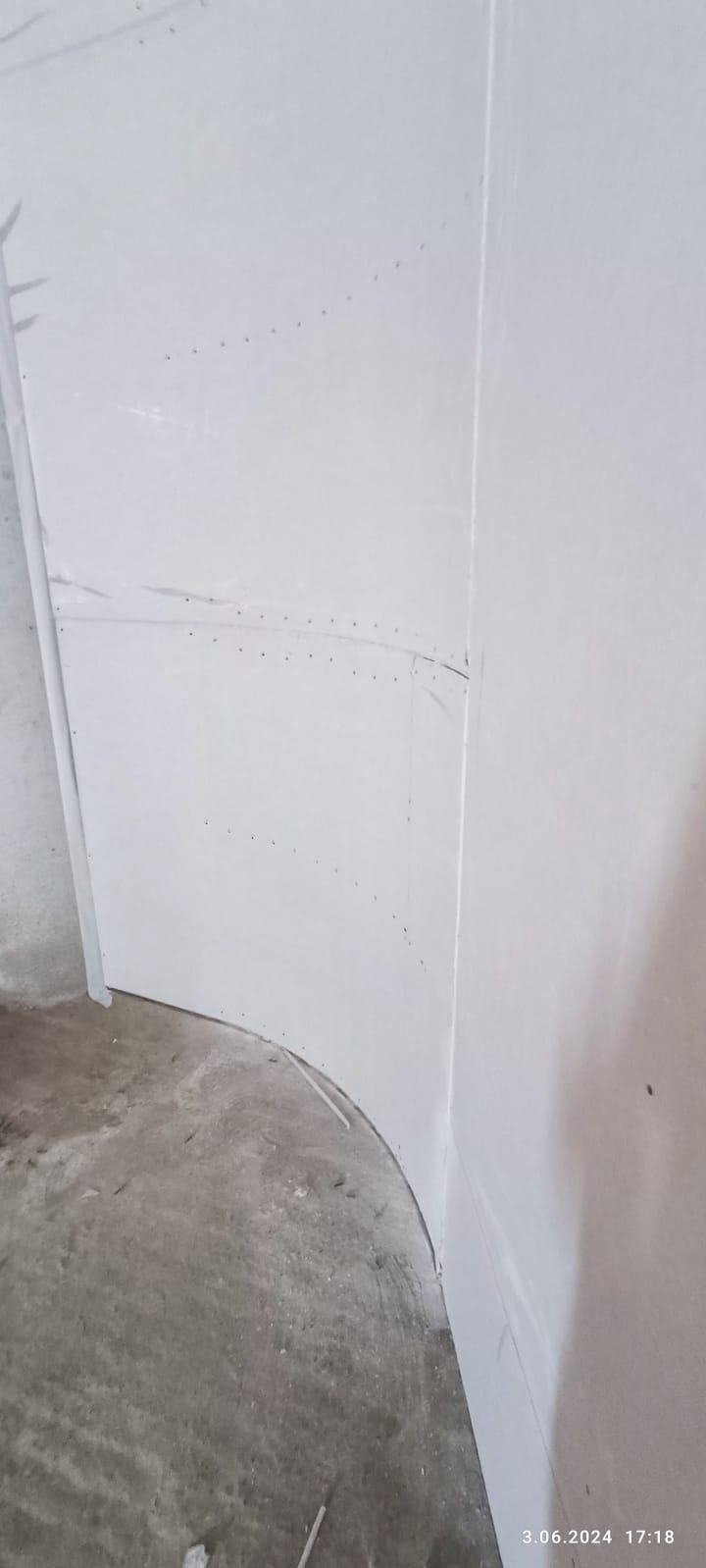 Krawędź ściany z płyt kartonowo-gipsowych, wykończona na łuku, widoczne ślady szpachlowania i mocowania. Surowy beton na podłodze, etap prac wykończeniowych.