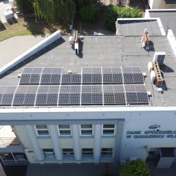 ZUEA BIAŁOWSKI - Widok z góry na budynek banku z panelami słonecznymi na dachu. Widoczne klimatyzatory, kominy i elementy instalacji. Część paneli odbija światło słoneczne.