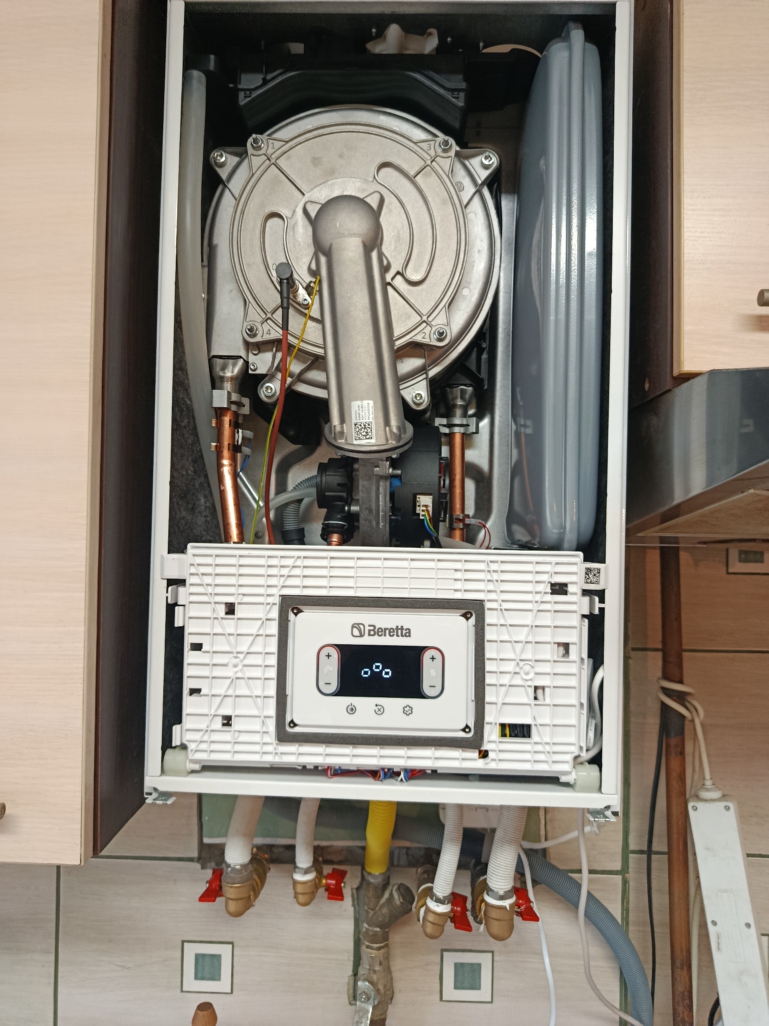 Kocioł gazowy Beretta w zabudowie, widoczne przyłącza wodne i gazowe z zaworami, panel sterowania i elementy wewnętrzne. Oświetlenie górne.