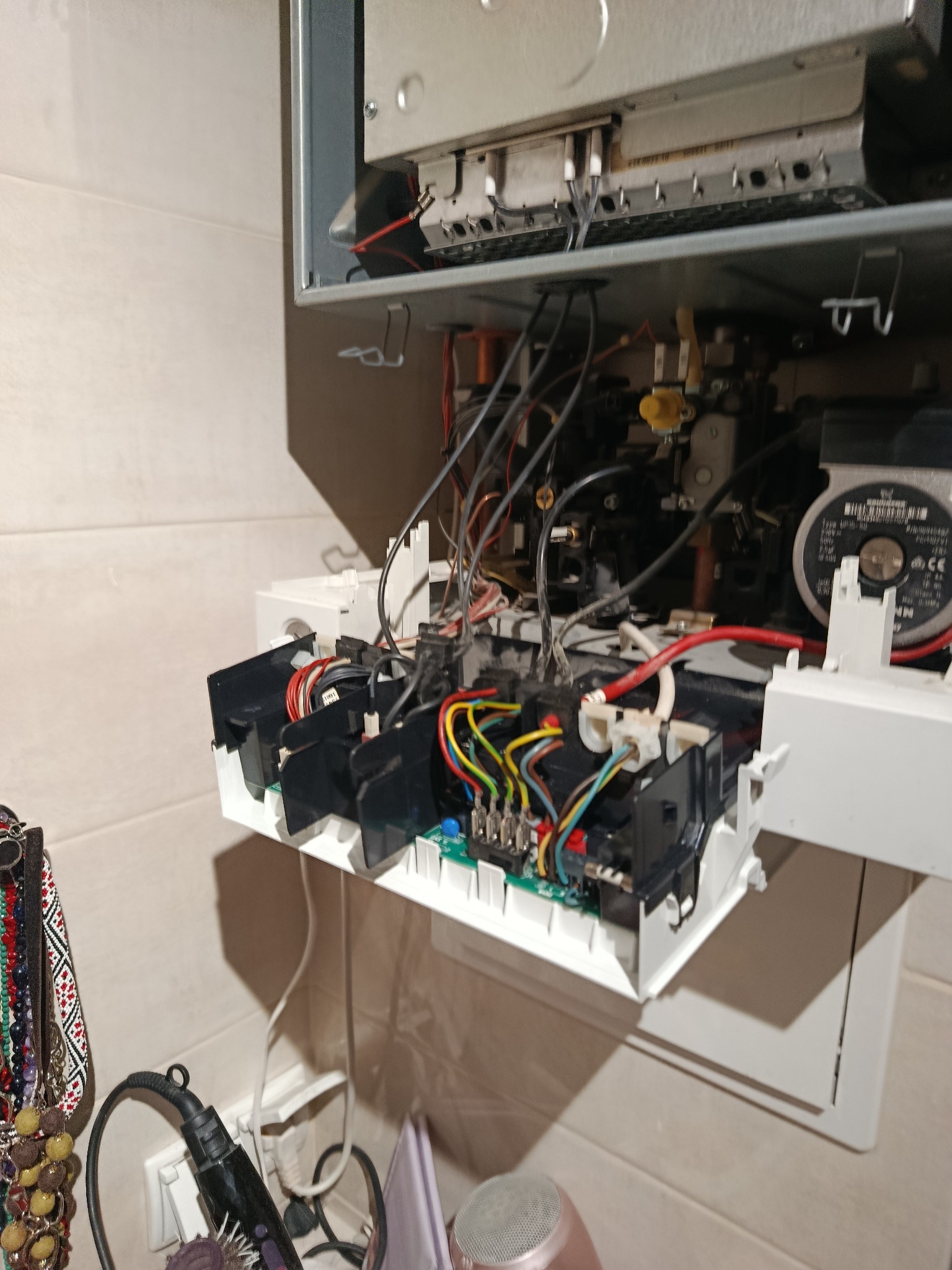 Otwarty piec gazowy z widocznymi przewodami i elementami elektronicznymi podczas serwisu. Widoczne narzędzia i akcesoria w tle.