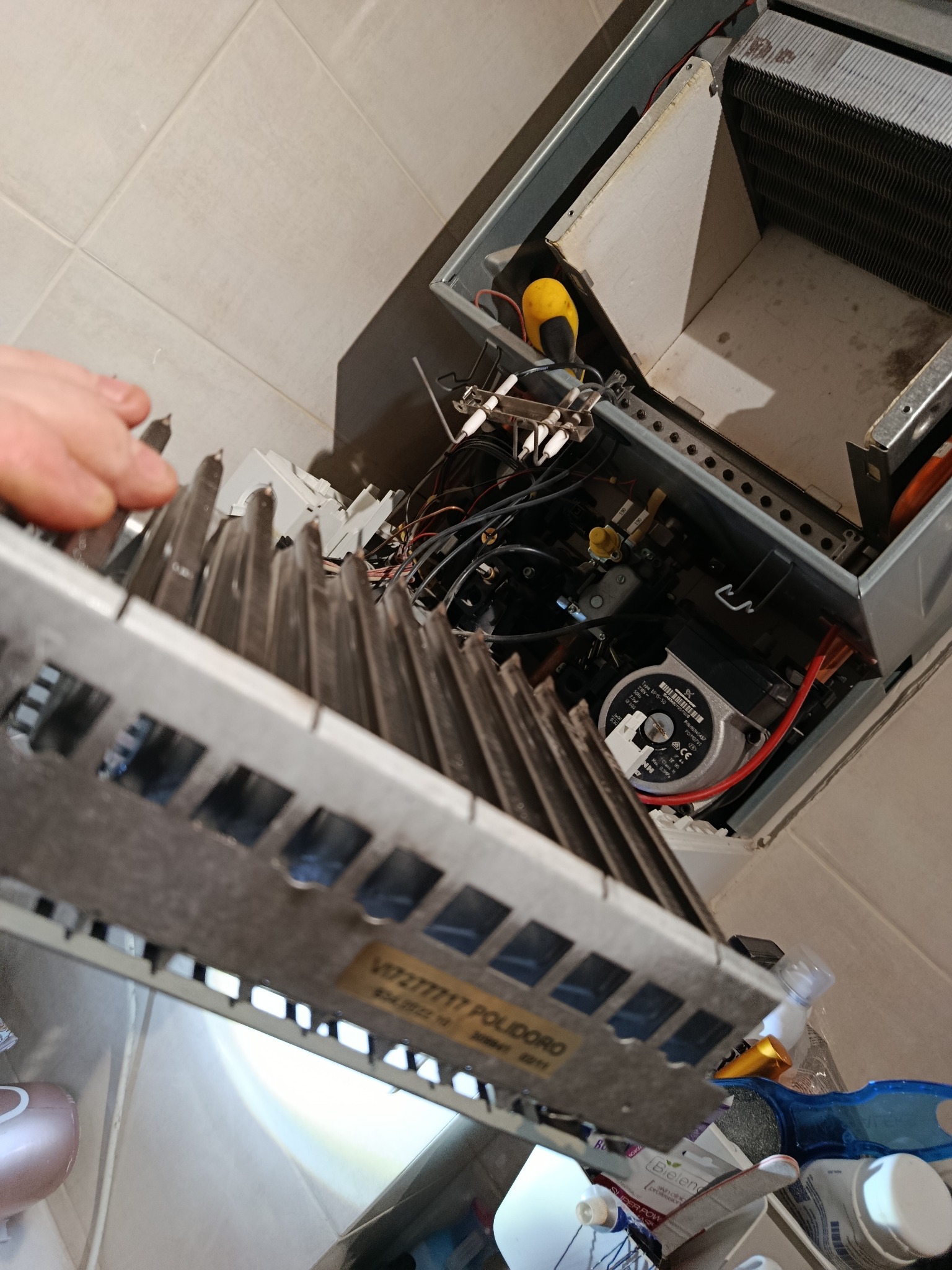 Otwarty piec gazowy z widocznymi elementami wewnętrznymi, w tym pompą obiegową i przewodami, podczas serwisu. Widoczne narzędzia i części zamienne.