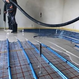 UdelemeTo s.r.o. - Wylewka samopoziomująca na ogrzewaniu podłogowym, widoczne niebieskie rurki i wylewka w trakcie rozprowadzania. Prace wykończeniowe w nowym budownictwie.