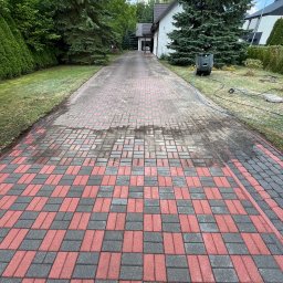 Bartłomiej Wojda - Częściowo umyta, czerwono-szara kostka brukowa na podjeździe, z widocznym urządzeniem wysokociśnieniowym i śladami wody. Tło stanowią drzewa i budynek.