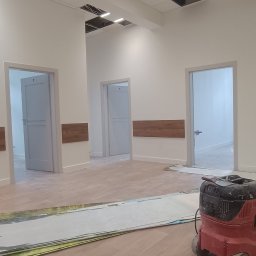 Taras Bulba Company - Wnętrze biura po malowaniu ścian na biało, z widocznym odkurzaczem przemysłowym i elementami sufitu podwieszanego w trakcie montażu. Widoczne trzy drzwi.