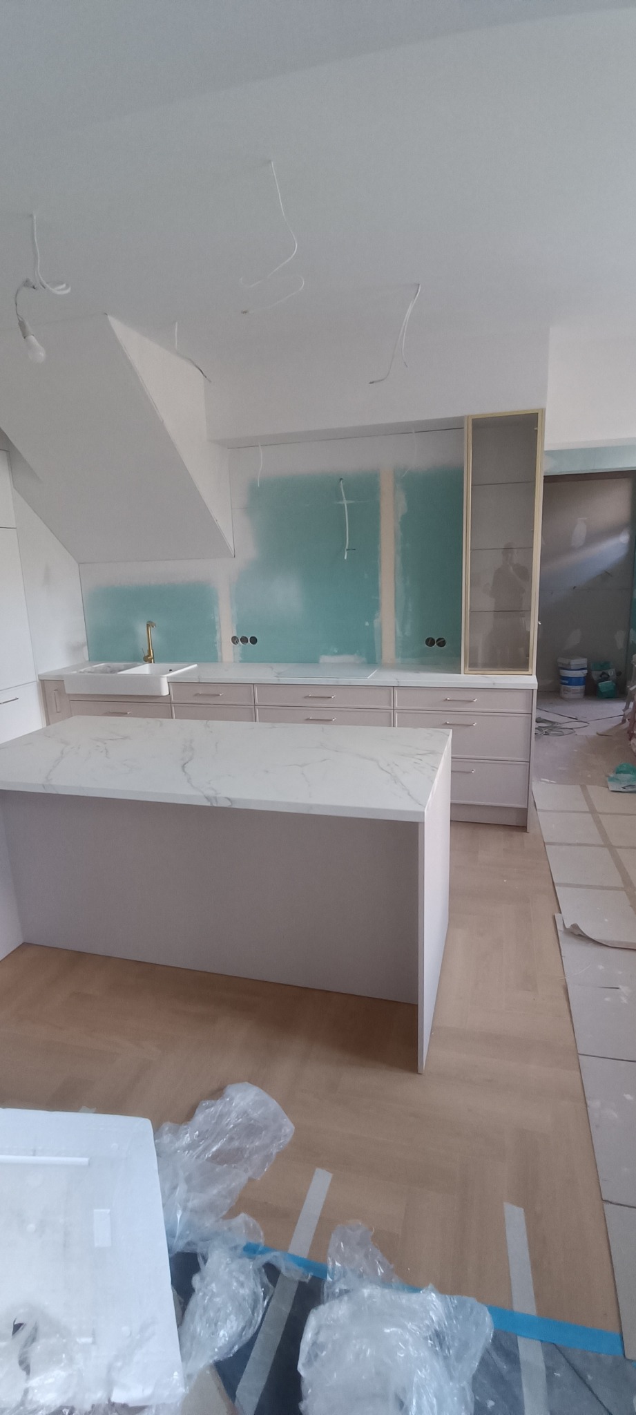 Kuchnia w trakcie remontu: wyspa z marmurowym blatem, zabudowa meblowa w pastelowych odcieniach, ściany przygotowane pod malowanie, widoczne instalacje elektryczne.