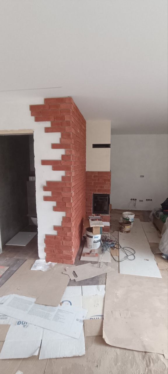 Fragment ściany z dekoracyjną cegłą w trakcie montażu. Widoczne narzędzia i materiały budowlane. Cegła ułożona w nietypowy, schodkowy wzór.