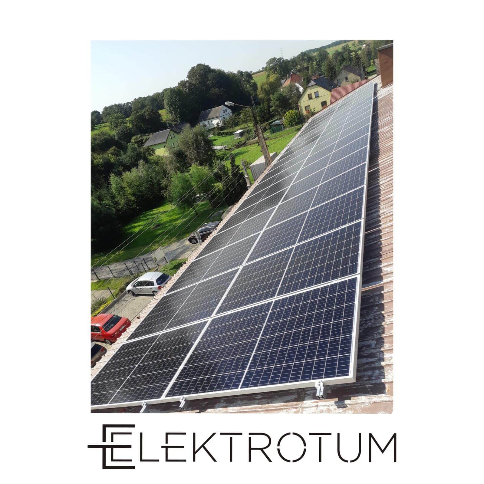 Panel słoneczny na dachu domu, widok z góry, w tle zieleń i zabudowania. Logo firmy w dolnej części kadru.