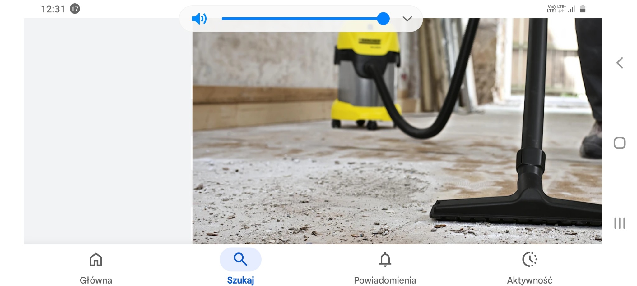 Żółto-srebrny odkurzacz przemysłowy Karcher i czarna ssawka na betonowej podłodze w trakcie sprzątania. Widok z ekranu smartfona.