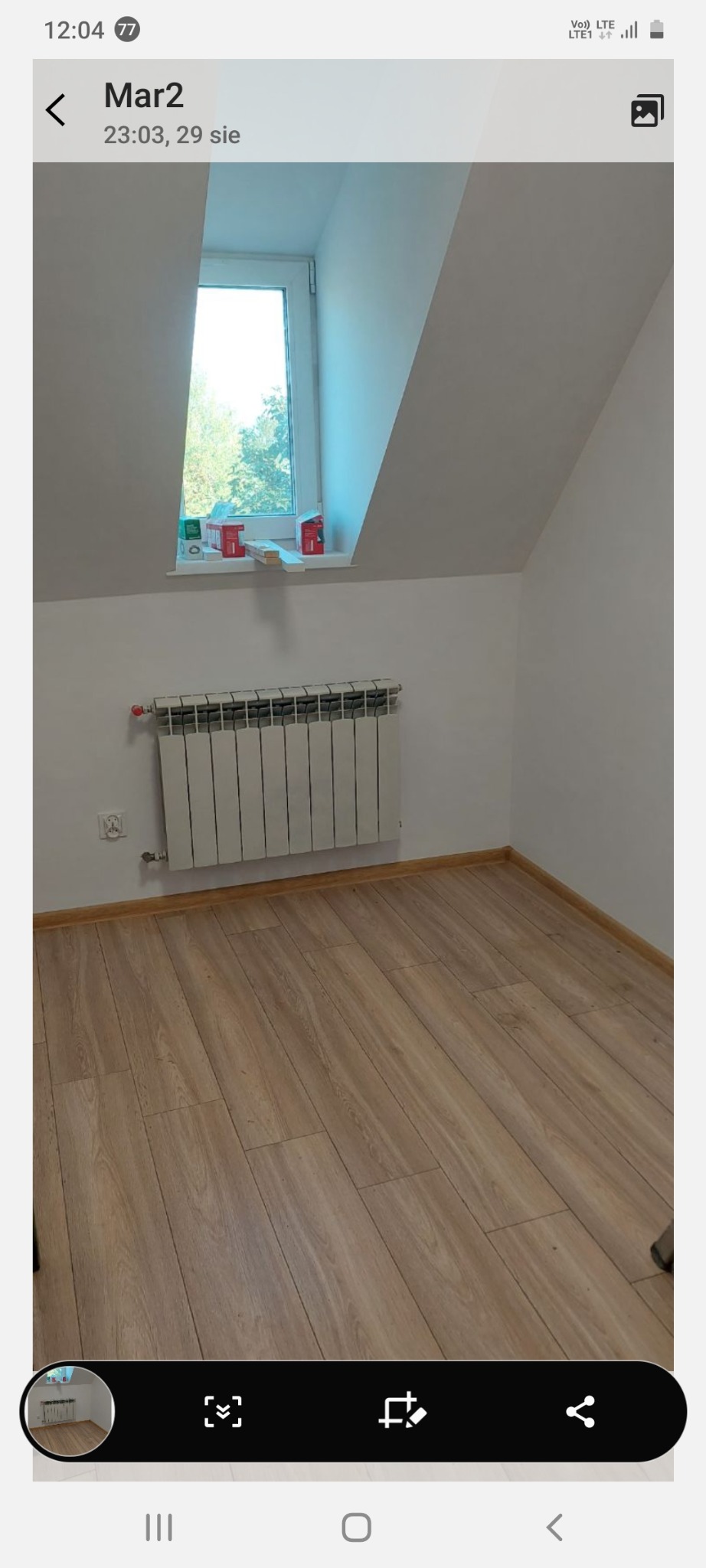 Poddasze z oknem, grzejnikiem i panelami podłogowymi. Świeżo wysprzątane, gotowe do użytku. Widok na zieleń za oknem.